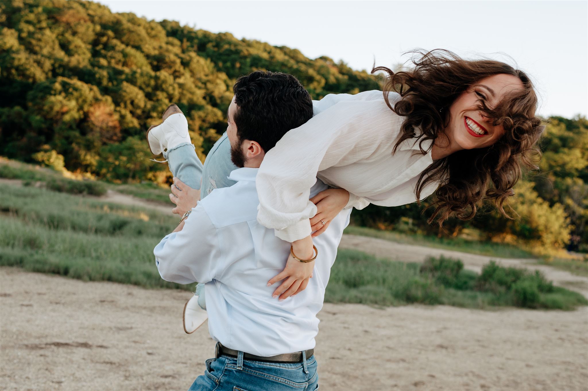 playful couple at park laughing together as bride is carried